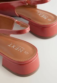 Punaiset patentti sandaalit, joissa on slingback-muotoilu, teksturoitu pinta ja paksu lohkareikä, ruskealla pohjalla ja brändätyllä sisäpohjalla.