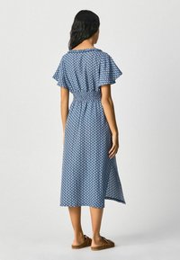 Modrá šatová šaty se zkrácenými volánkovými rukávy, elastickým pasem a délkou po lýtka. Vyrobeno z lehké tkaniny s geometrickým vzorem.