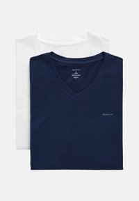 Zwei V-Ausschnitt-T-Shirts übereinander gestapelt: eines in Marineblau, eines in Weiß. Beide haben kurze Ärmel und das "GANT"-Logo auf der Vorderseite. Aus Baumwollmaterial.