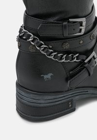 Schwarze Lederstiefel mit silbernem Kettendetail, mehreren Riemen mit Schnallen und einem dezenten Pferdelogo an der Seite. Texturierte Oberfläche.