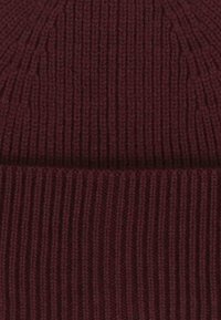 Căciulă tricotată burgundy cu textură cu nervuri verticale, având un design de țesătură netedă și elastică. Fără accesorii sau detalii vizibile.