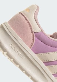 Gros plan sur le talon de baskets roses et beiges avec des textures en daim et en cuir, panneau latéral en tissu violet, et "Cloudfoam" embossé sur la semelle blanche.