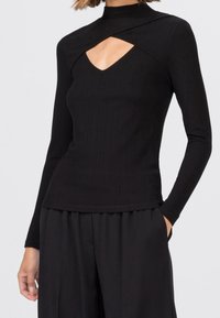 Svart ribbad långärmad tröja med hög halsringning och utskärningsdetalj, med en figurnära design och slät textur.