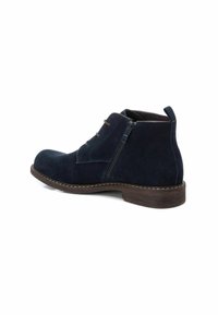 Botas de ante azul marino a la altura del tobillo con punta redonda, cremallera lateral y suela marrón contrastante. Incluyen cordones y una tira en la parte posterior para facilitar su uso.