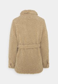 Veste en polaire beige, douce et duveteuse, avec une taille ceinturée, un col et des poches latérales. Texture douce et coupe décontractée, conçue pour la chaleur et le confort.