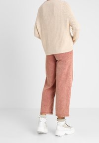 Přesně padnoucí pletený svetr v béžové barvě v oversized stylu, spárovaný s růžovými širokými kordovými kalhotami a bílými platformovými teniskami s šedými tkaničkami a texturovanými detaily.