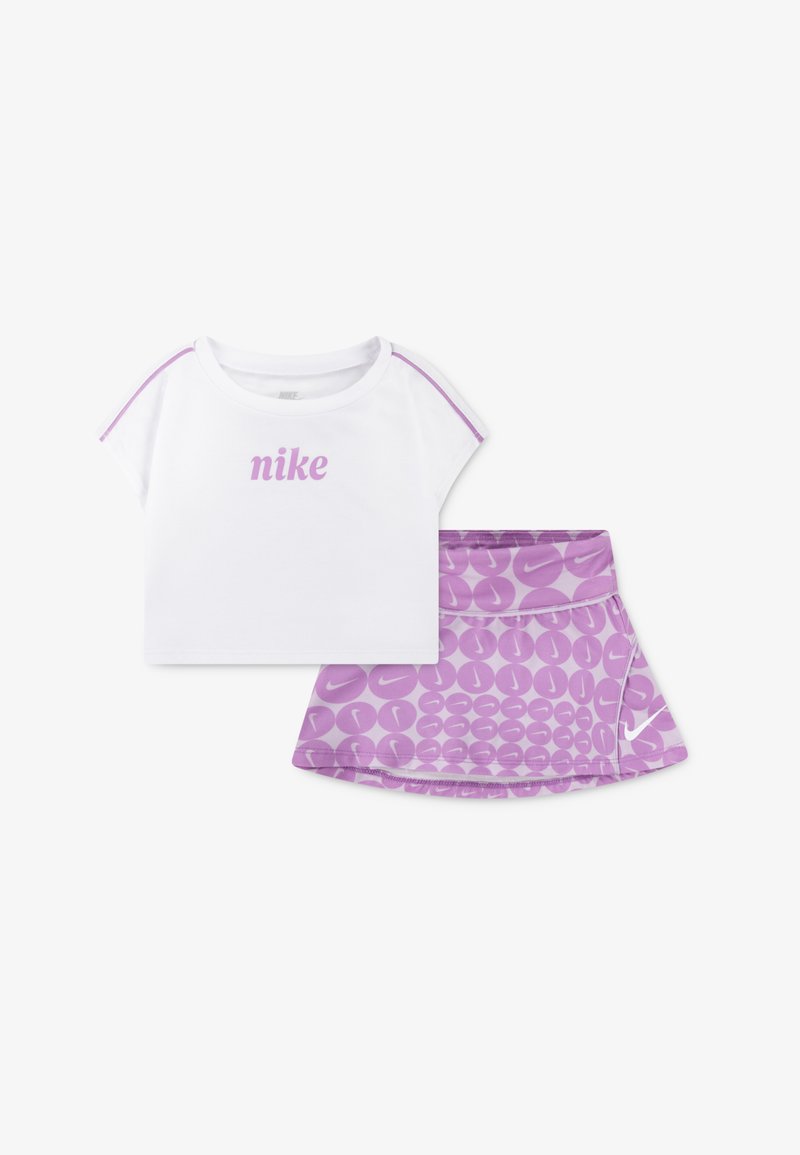 Λευκό κοντομάνικο T-shirt με λευκή λογότυπο "Nike" και περιθώριο σε μοβ χρώμα, συνδυασμένο με μοβ φούστα που διαθέτει κυκλικό σχέδιο και λογότυπο.