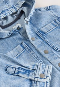 Hellblaue Jeansjacke mit Metall-Druckknöpfen, Brusttaschen und sichtbaren Nahtdetails.