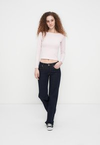 Ροζ ανοιχτόχρωμο crop top με μακριά μανίκια συνδυασμένο με σκούρο μπλε τζιν παντελόνι με φαρδιά μπατζάκια. Το σύνολο ολοκληρώνεται με μαύρα αθλητικά παπούτσια με λευκές λεπτομέρειες.