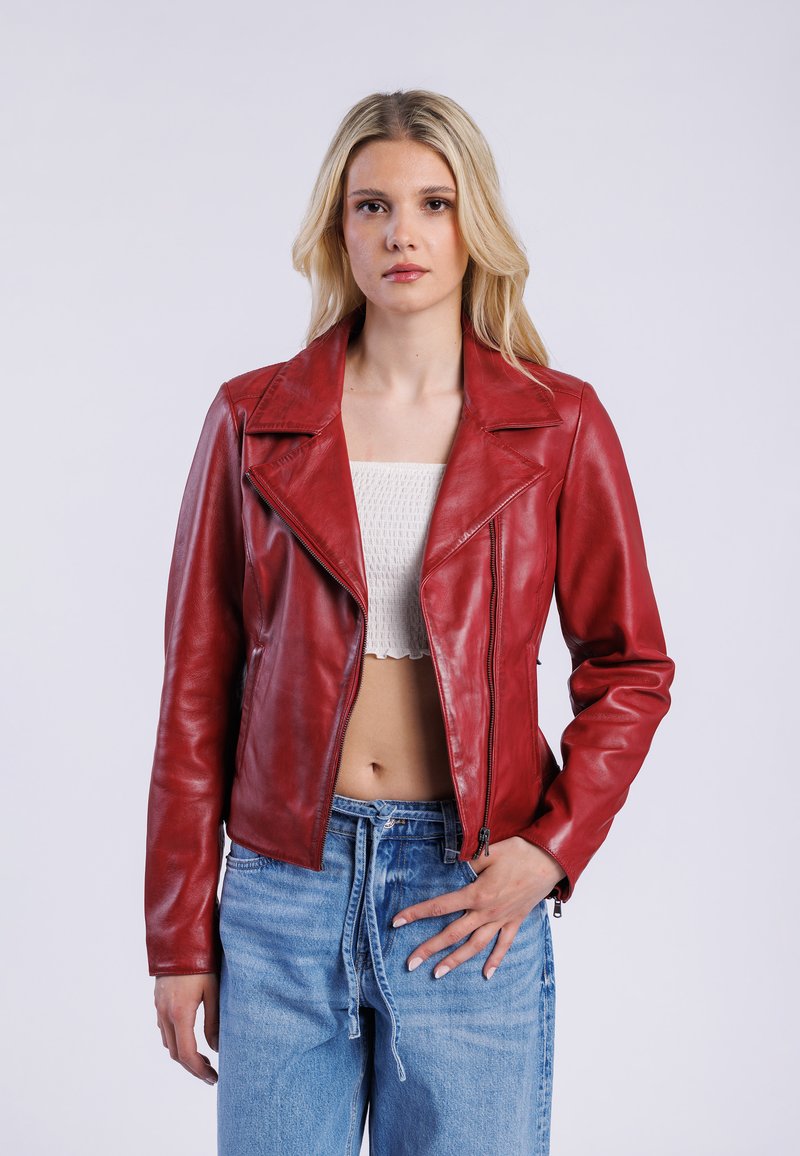 Červená kožená motorkářská bunda s klopovým límcem, zapínáním na zip a dlouhými rukávy. Kombinována se světlými modrými džínami s oděrkami.