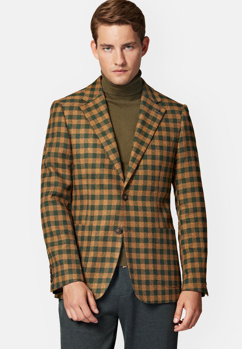 Brązowa i zielona marynarka w kratę z klapami o prostym kroju, z jednym guzikiem i teksturowanym materiałem. Noszona na ciemnym golfie.