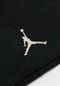 Musta neulepipo, jossa on teksturoitu pinta, ja etupuolella hopeinen Jumpman-logo, joka kuvaa pelaajaa hyppyposeerauksessa.