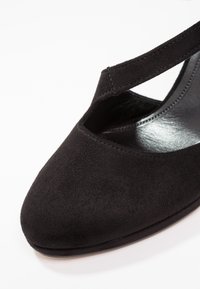 Chaussure à talon haut en daim noir avec un bout pointu et un design à brides croisées, dotée d'une doublure intérieure lisse et brillante.