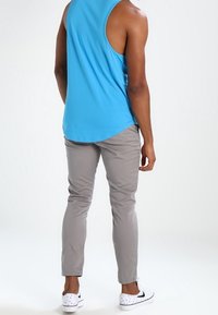 Niebieska bezrękawnikowa koszulka na ramiączkach, szare spodnie o wąskim kroju oraz białe trampki w czarne kropki. Gładka tkanina i dopasowany krój, bez widocznych wzorów.