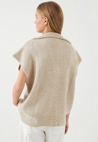 Lys beige strikket sweater med ribbet struktur, der har en sjalskrave og korte ærmer. Blød, afslappet pasform.