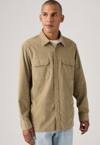 Tan corduroy shirt met een button-down kraag, twee borstzakken en een relaxte fit. Heeft een subtiele ribbeltextuur.