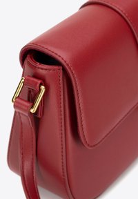 Borsa a tracolla in pelle rossa con una texture liscia, forma arrotondata e un dettaglio di fibbia in oro sulla tracolla regolabile.