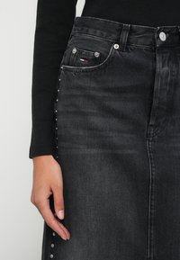 Zwarte denim rok met zilveren hardware, zijstiften en een klassiek ontwerp met vijf zakken. De stof heeft een lichte textuur en verweerde details.