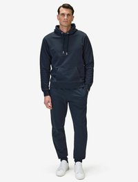 Marinblå hoodie med dragsko och framficka, matchad med joggers och vita sneakers. Slät textur, avslappnad design.