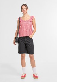 Top senza maniche a fiori rossi con collo arricciato, abbinato a pantaloni corti in denim scuro con orli sfrangiati, calzini bianchi e sneakers rosse.