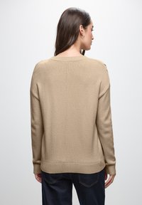 Maglione beige lavorato a maglia con scollo rotondo, polsini e orlo a costine. Il tessuto è texturizzato e il design presenta una vestibilità rilassata.