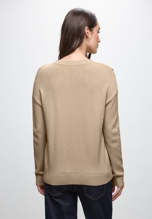 Maglione beige lavorato a maglia con scollo rotondo, polsini e orlo a costine. Il tessuto è texturizzato e il design presenta una vestibilità rilassata.