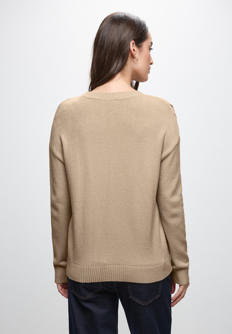 Maglione beige lavorato a maglia con scollo rotondo, polsini e orlo a costine. Il tessuto è texturizzato e il design presenta una vestibilità rilassata.