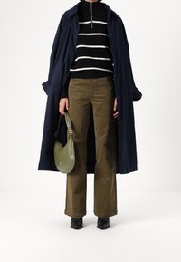 Manteau trench-coat marine, pull en maille rayé noir et blanc, pantalon en velours côtelé vert olive, sac à main léger vert, bottines noires.