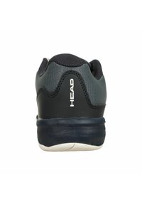 Zapatilla deportiva negra y gris con parte superior de malla, talón acolchado, suela de goma y logo blanco en la parte trasera, diseñada para comodidad y soporte.