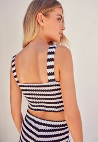 Černo-bílý pruhovaný crop top s širokými ramínky a čtveratým designem na zádech, vyrobený z texturovaného pleteného materiálu.