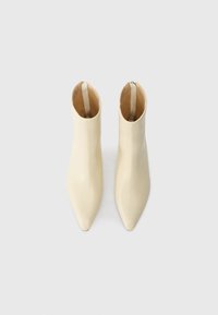 Bottines crème avec une finition brillante, bout pointu et fermeture éclair à l'arrière, présentant un design épuré et minimaliste.