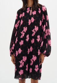 Svart och rosa blommönstrad plisserad klänning med nyckelhålsringning och voluminösa ärmar, med en flytande tygtextur.