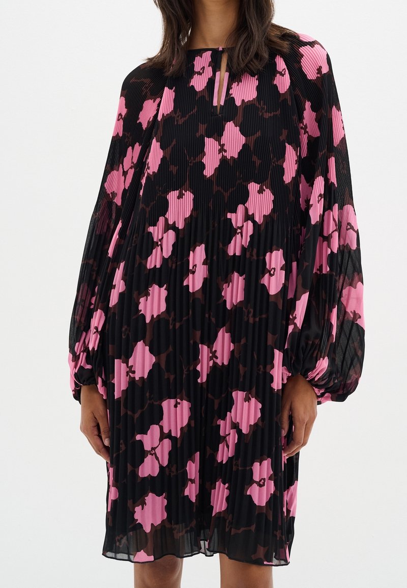 Svart och rosa blommönstrad plisserad klänning med nyckelhålsringning och voluminösa ärmar, med en flytande tygtextur.