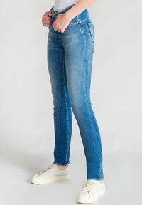 Jeans skinny en denim bleu clair, avec une taille haute, un léger effet de décoloration et un design à cinq poches. Portés avec des baskets blanches.