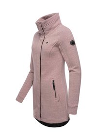 Veste rose clair avec un col haut, texture douce, zips sur les côtés et un accent noir sur la manche. Présente un dos plus long pour plus de couverture.