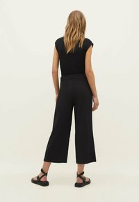 Svarta korta vida byxor med elastisk midja och slät yta, i kombination med en figurnära svart topp och svarta sandaler.