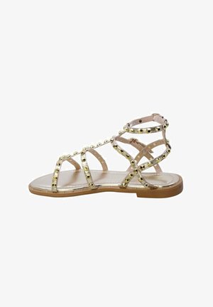 Sandalo piatto beige con molteplici sottili cinturini decorati con borchie dorate e chiusura alla caviglia con fibbia.