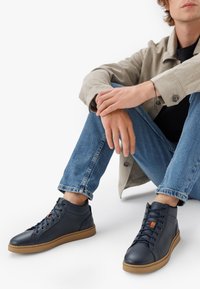 Tumes kõrge säärega jalatsid, valmistatud tekstuuritud nahast, pruunide kummitaldadega, ümmarguste varvastega ning paeltele aktsentvärviga, mõeldud igapäevaseks kandmiseks.