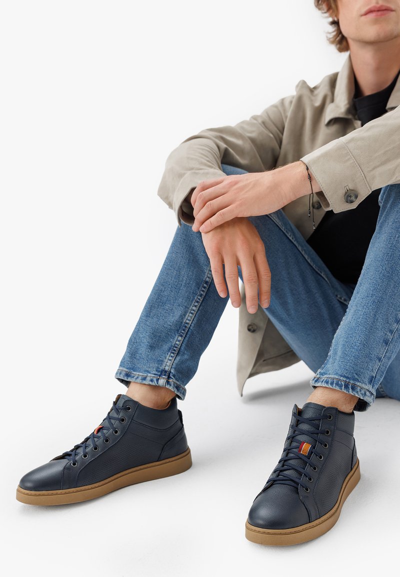 Tumes kõrge säärega jalatsid, valmistatud tekstuuritud nahast, pruunide kummitaldadega, ümmarguste varvastega ning paeltele aktsentvärviga, mõeldud igapäevaseks kandmiseks.