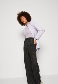Lilla blazer over en lys lilla topp, paret med høyt liv sorte blanke vide bukser. Teksturert stoff og strømlinjeformet design.