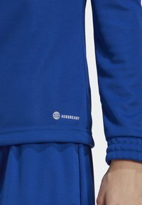 Camiseta deportiva de manga larga azul hecha de tejido texturizado, con puños acanalados y un logo "AEROREADY" en blanco en el dobladillo inferior.