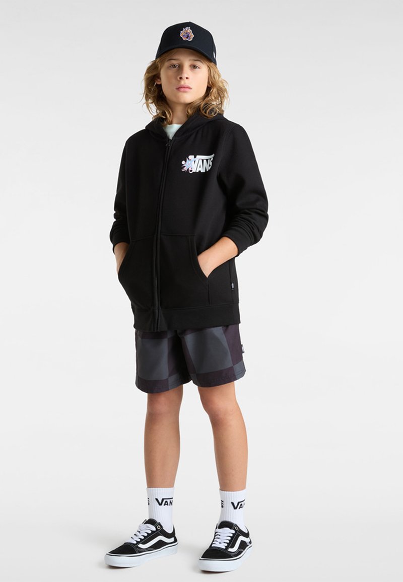 Sudadera con cremallera negra con el logotipo de Vans, combinada con pantalones cortos grises estampados, zapatillas negras de Vans y calcetines blancos con la marca Vans.