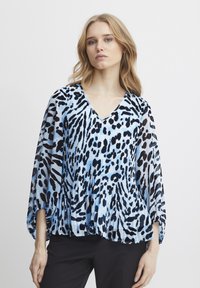 Blusa plissettata di colore azzurro chiaro con stampa astratta di animali in nero e blu navy, con scollatura a V e maniche ampie, realizzata in un materiale leggero.