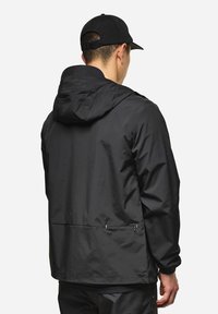 Giacca impermeabile nera con cappuccio, superficie liscia, dotata di polsini elastici e due tasche con zip sul retro.