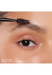 Brow Freeze® applicator met een zwarte, spiraalvormige borstel, gestyled tegen een close-up van een wenkbrauw en ooglid op een gladde huid.