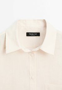 Crèmefarvet skjorte med pointekrave, to synlige knapper og en sort Massimo Dutti-etiket indeni halsudskæringen.