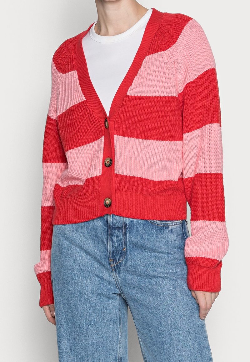 Rood en roze gestreepte cardigan met een V-hals, knoopsluiting, geribbelde textuur en lange mouwen, gecombineerd met high-waisted spijkerbroeken.