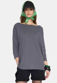 Szara, luźna bluzka z długim rękawem i szerokim dekoltem, stylizowana z czarnymi szortami. Dodatki to czapka w kolorze czarnym oraz zielony szalik w wzory.