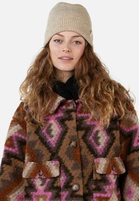 Colorful patterned woolen jacket in brown, pink, and cream with a collar, two front pockets, and wooden buttons. Beanie hat in beige.