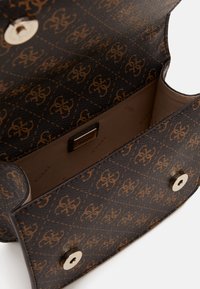 Brown and black patterned Guess handbag with magnetic snap closure, open to show beige fabric interior and logo plaque inside.